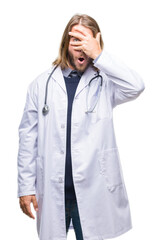 Canvas Print - Young handsome doctor man with long hair over isolated background peeking in shock covering face and eyes with hand, looking through fingers with embarrassed expression.