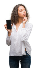 Sticker - Young hispanic woman using smartphone serious face thinking about question, very confused idea