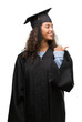 © Krakenimages.com - Young hispanic woman wearing graduation uniform pointing and showing with thumb up to the side with happy face smiling