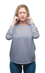 Wall Mural - Young blonde woman over isolated background covering ears with fingers with annoyed expression for the noise of loud music. Deaf concept.