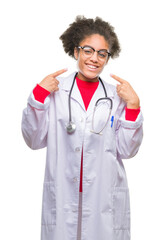 Wall Mural - Young afro american doctor woman over isolated background smiling confident showing and pointing with fingers teeth and mouth. Health concept.