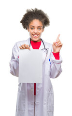 Sticker - Young afro american doctor woman holding blank paper over isolated background surprised with an idea or question pointing finger with happy face, number one