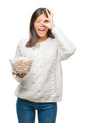 Canvas Print - Young asian woman eating popcorn over isolated background with happy face smiling doing ok sign with hand on eye looking through fingers