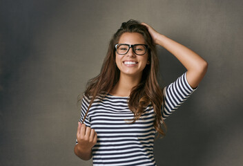 Woman, glasses and portrait with confidence, optometry and playful on gray studio background. Female person, face and happy for eyewear, sight and smile with casual outfit, clear vision and wellness