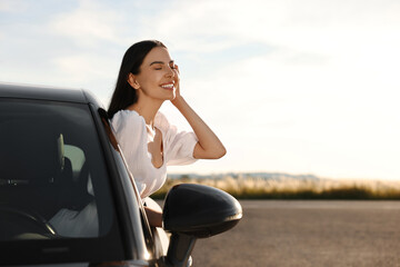 Canvas Print - Smiling young woman leaning out of car window outdoors. Enjoying trip