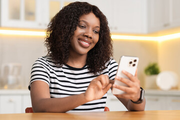 Wall Mural - Beautiful woman using mobile phone at table indoors