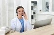 © New Africa - Professional receptionist working at wooden desk in hospital