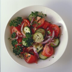 A fresh vegetable salad with slices of cucumber, tomato, and red onion in a white bowl, accented with parsley and a light seasoning of pepper.