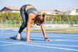 © damianobuffo - Athletic woman prepares to sprint on a blue track under the summer sun, embracing outdoor fitness