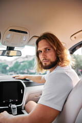 Wall Mural - Young man with long hair sitting in car interior with thoughtful expression