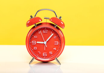 Red alarm clock on white table on yellow background.