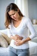 © Iryna - A young woman is holding her stomach with her hands due to sharp pain, abdominal pain