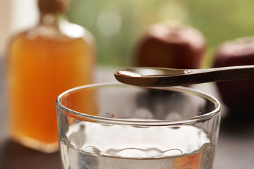 Apple cider vinegar on a wooden spoon above a cup of water.