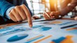 © capuchino009 - Business Data Analysis: Close-up of hands pointing at charts and graphs during a strategy meeting.