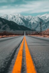 Wall Mural - Wide open road stretches towards snow-capped mountains under a cloudy sky