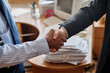 © pressmaster - Two professionals completing business handshake in corporate office environment with paperwork on table, symbolizing agreement and partnership between individuals in business