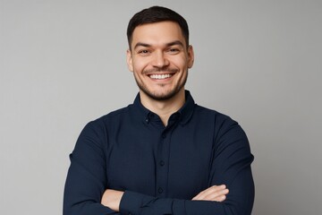 Smiling man with folded arms in a dark blue shirt, posing confidently against a grey background, ideal for advertising and web design. High-resolution portrait with a professional andapproachable look