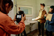 © pressmaster - Several people are working on a film set with various equipment in a bathroom environment holding a script and adjusting lighting angles. Set appears busy with activity and focus