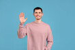 © New Africa - Happy young man waving on light blue background