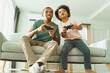 © eggeeggjiew - Black African American Father and son sitting on couch playing video games with controllers. Family time and bonding concept.