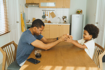 Wall Mural - Black African American Father and son playing a hand game at home kitchen table. Casual home lifestyle. Family bonding and playful activities concept.