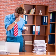 Wall Mural - Young employee with excessive work sitting at the office