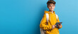© spyrakot - Tech-Savvy Schoolboy in Yellow Hoodie Holding Digital Tablet Against Blue Background for Educational Purposes