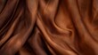 © vadosloginov - A brown fabric with a subtle pattern is draped in soft, flowing folds, creating a smooth and textural background. The fabric's texture and light play on the surface, creating a sense of depth and move
