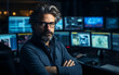 © imagineRbc - A man with glasses and a beard stands in front of a computer monitor with a serious expression on his face
