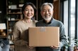 © kinara art design - Happy Asian senior couple holding a cardboard box, smiling at the camera, standing in their home.
