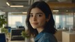 © Esmeralda - A young Hispanic woman in a stylish denim jacket smiles softly while working in a modern office, with greenery and computer screens in the background.