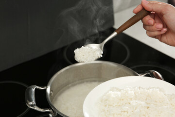 Canvas Print - Woman taking boiled rice from pot into plate, closeup