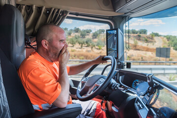 Wall Mural - Truck driver driving the truck on the highway and yawning in a clear gesture of tiredness and fatigue at the wheel.