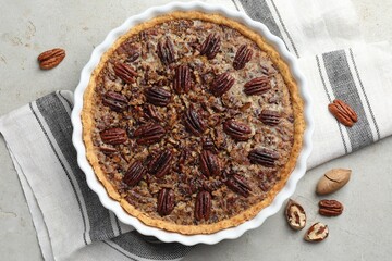 Wall Mural - Delicious pecan pie in baking dish and fresh nuts on gray textured table, top view