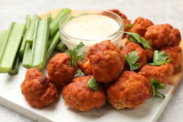 Baked cauliflower buffalo wings with celery and sauce on grey table, closeup