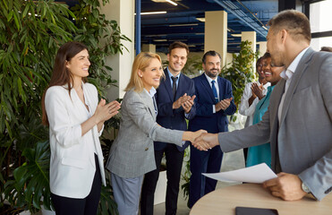 Company employees shaking hands celebrating success, making a deal, business achievement or signing a contract. Group of business people in office applauding to their coworkers on a meeting.