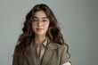 © cochisevisuals - Young woman with long curly brown hair wearing glasses and a brown blazer, looking at the camera.