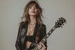 © cochisevisuals - Young woman in a black leather jacket plays an electric guitar, looking intense with long, windswept hair.