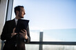 © Minerva Studio - Businessman using digital tablet smiling looking out office window