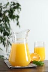 Wall Mural - Tasty orange juice in jug, glass and citrus fruit on wooden table