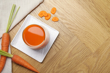 Wall Mural - Healthy juice in glass and fresh carrot on wooden table, flat lay. Space for text