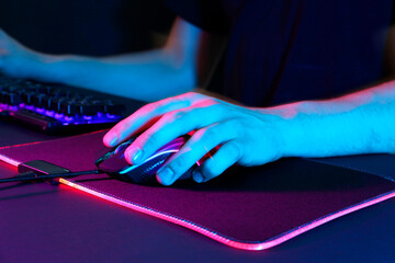 Wall Mural - Gamer using modern wired computer mouse in neon lights at dark table, closeup