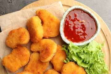 Wall Mural - Board with hot chili sauce, lettuce and nuggets on grey textured table, top view