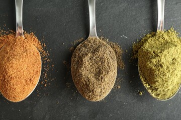 Different superfood powders in spoons on black table, flat lay