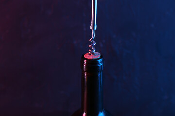 Canvas Print - Wine bottle with corkscrew in lights on dark background, closeup