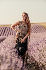 Wall Mural - A woman is standing in a field of purple flowers, wearing a black dress and a black hat.