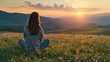 © Chandara - Latin woman sitting cross-legged on a grassy field, watching the sun set behind distant mountains, with a look of contentment and thanks.