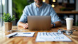 © khonkangrua - Businessman typing on a laptop at a wooden desk, with documents, coffee, and a small plant, symbolizing modern work and productivity.