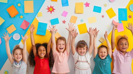 A group of enthusiastic elementary students with hands raised, surrounded by educational posters and classroom supplies. 