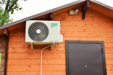 The external unit of a powerful air conditioner hangs on the wall of a wooden house